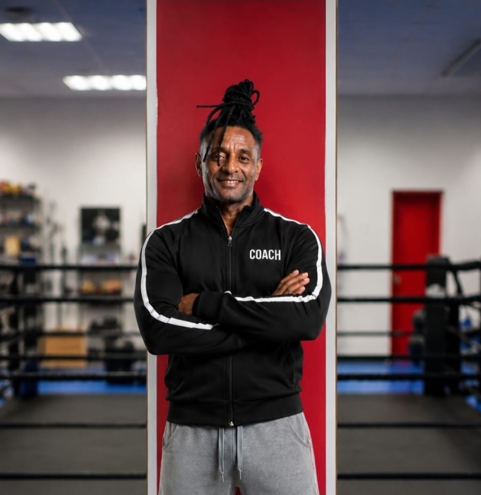 Coach Haile Tadese mit verschränkten Armen im Studio vor roter Säule